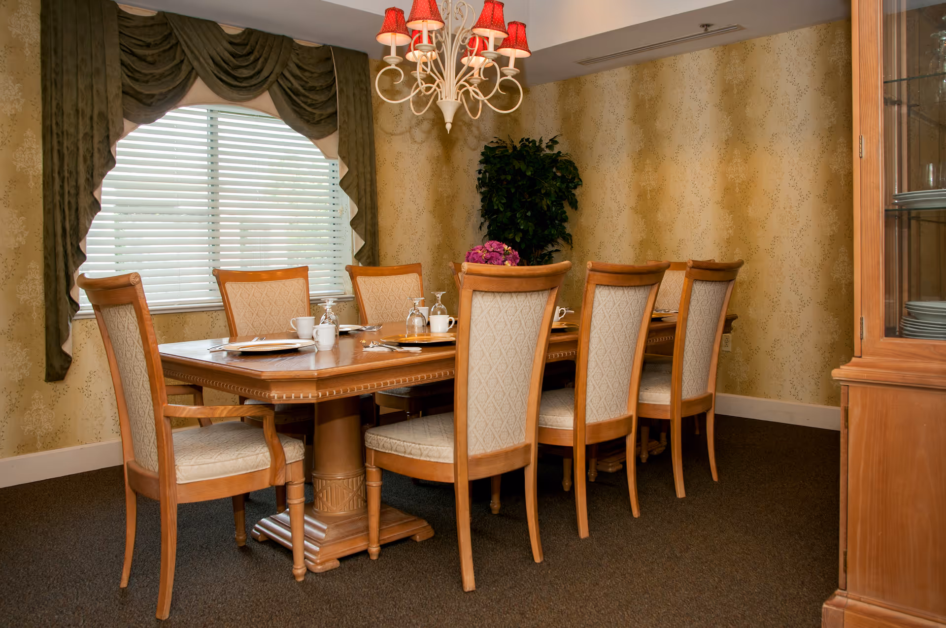 Formal dining room with a wooden table set for eight, upholstered chairs, a chandelier, and a window with green drapes.