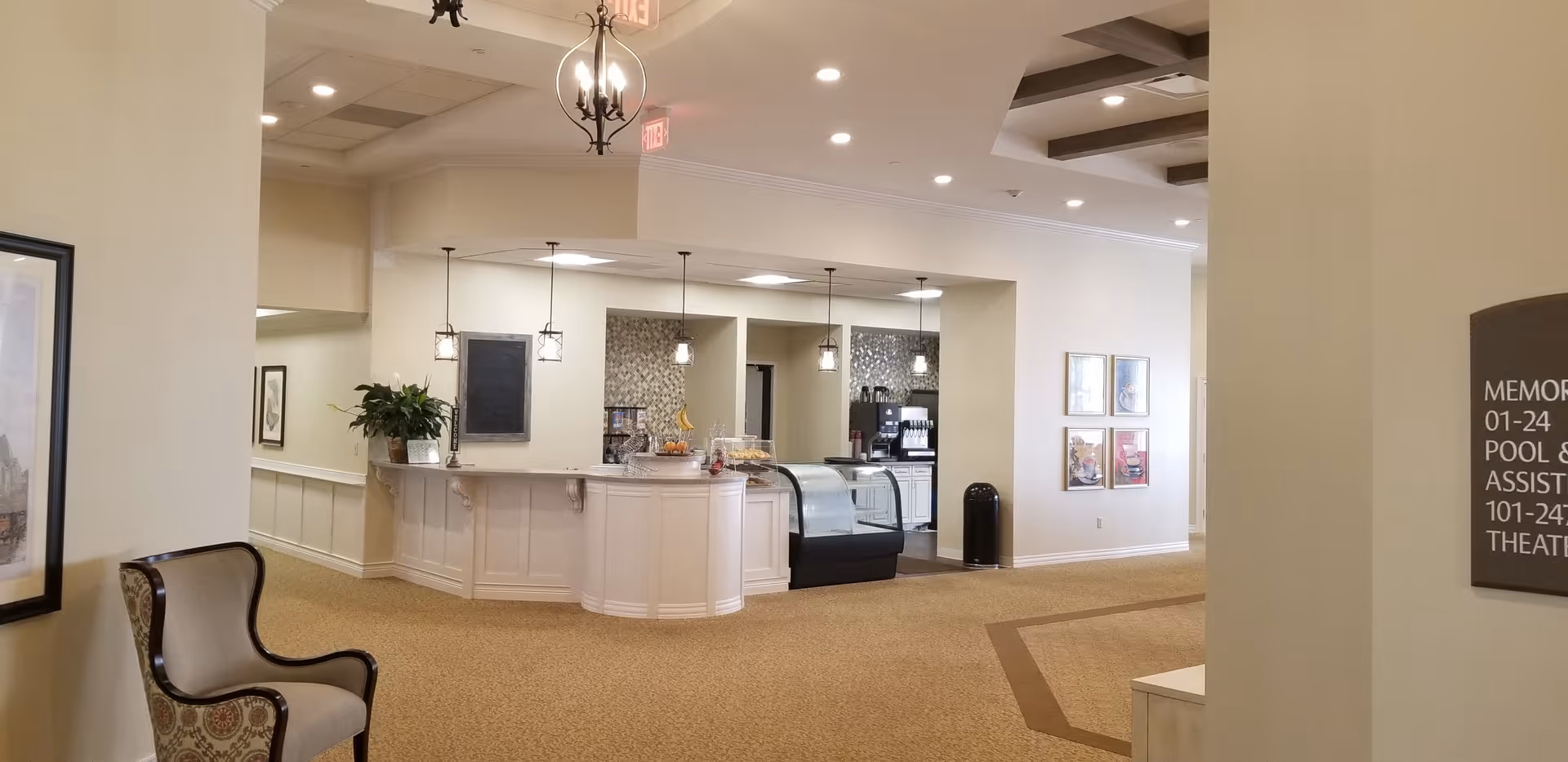 Bright interior lobby with a curved reception/snack counter and glass display case, pendant lights, carpeted seating area, and framed artwork.