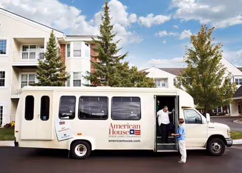 A white shuttle bus parked outside a multi-story senior living building.
