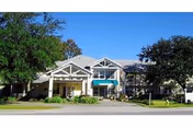 Exterior view of a single-story assisted living facility building with a covered entrance, surrounded by trees and greenery under a clear blue sky.