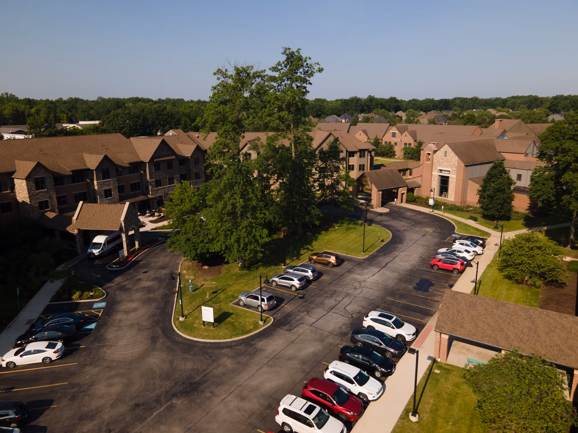 Aerial view of a senior living complex with brick buildings, trees, driveways, and parked cars.