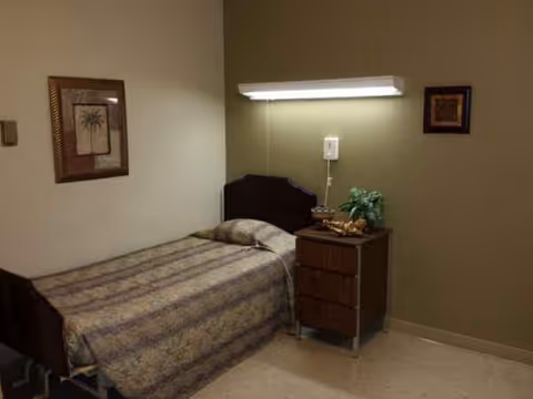 A single bed with a patterned quilt, nightstand, plant, and framed art in a bedroom.