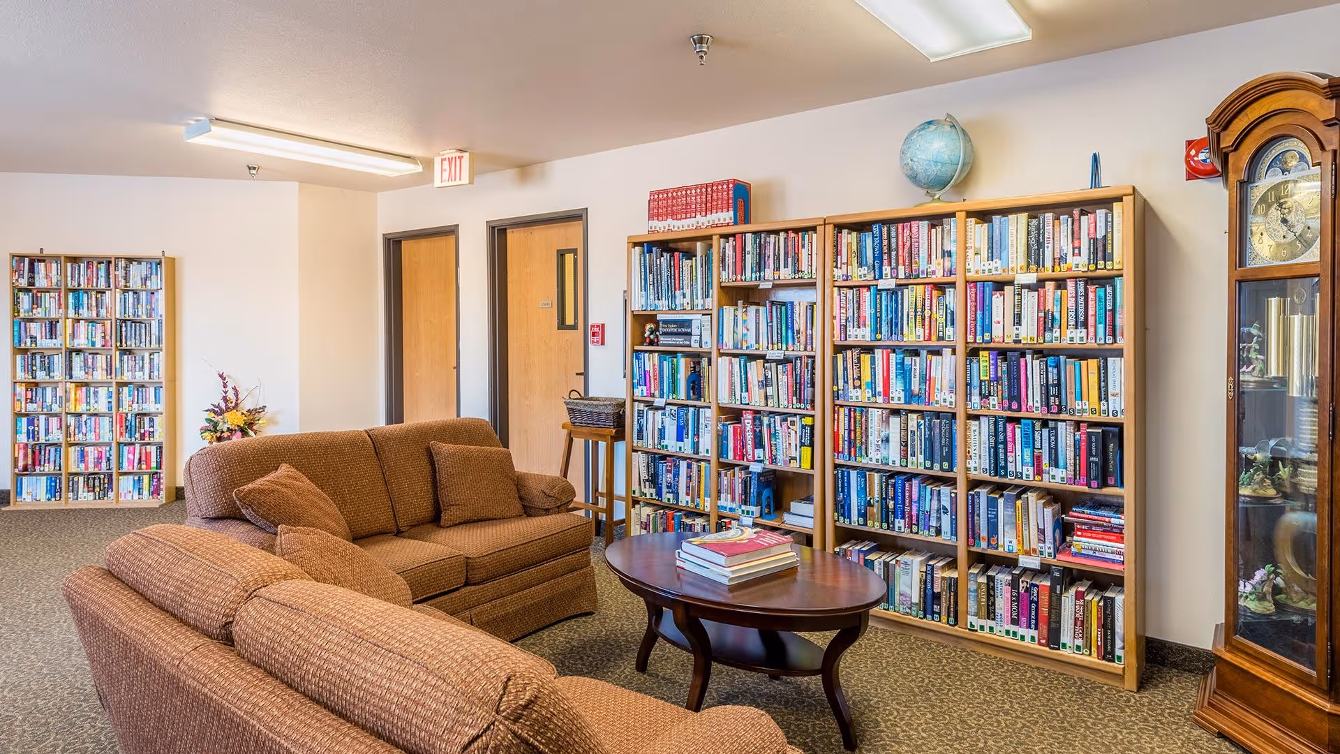 A cozy lounge/library with two sofas, a coffee table, and wall-length bookshelves filled with books.