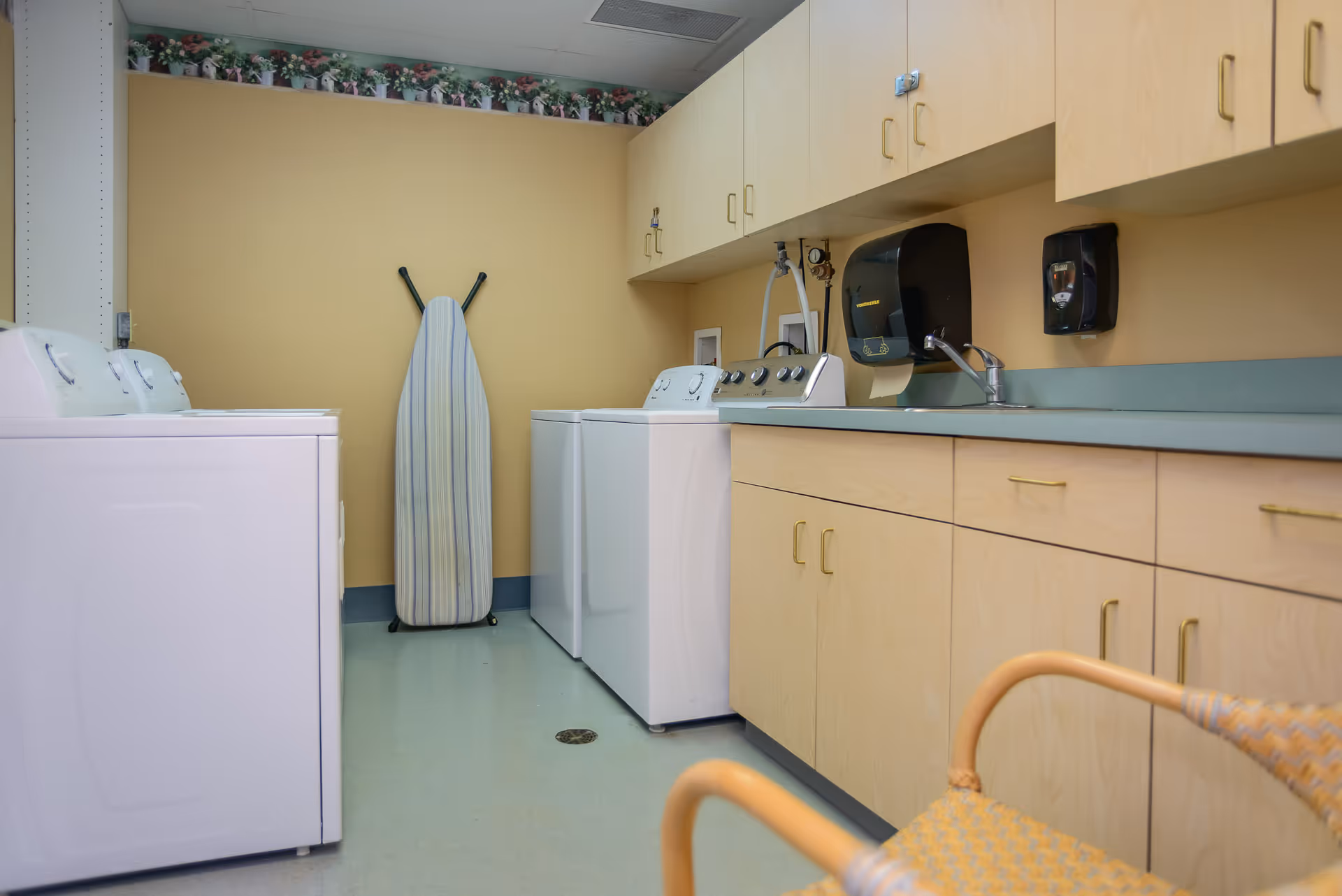 Laundry room featuring washing machines and a dryer, an ironing board, a sink, and storage cabinets.