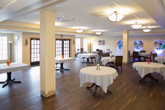 Spacious dining room with round tables covered in white tablecloths, chairs, and decorative wall aquariums.