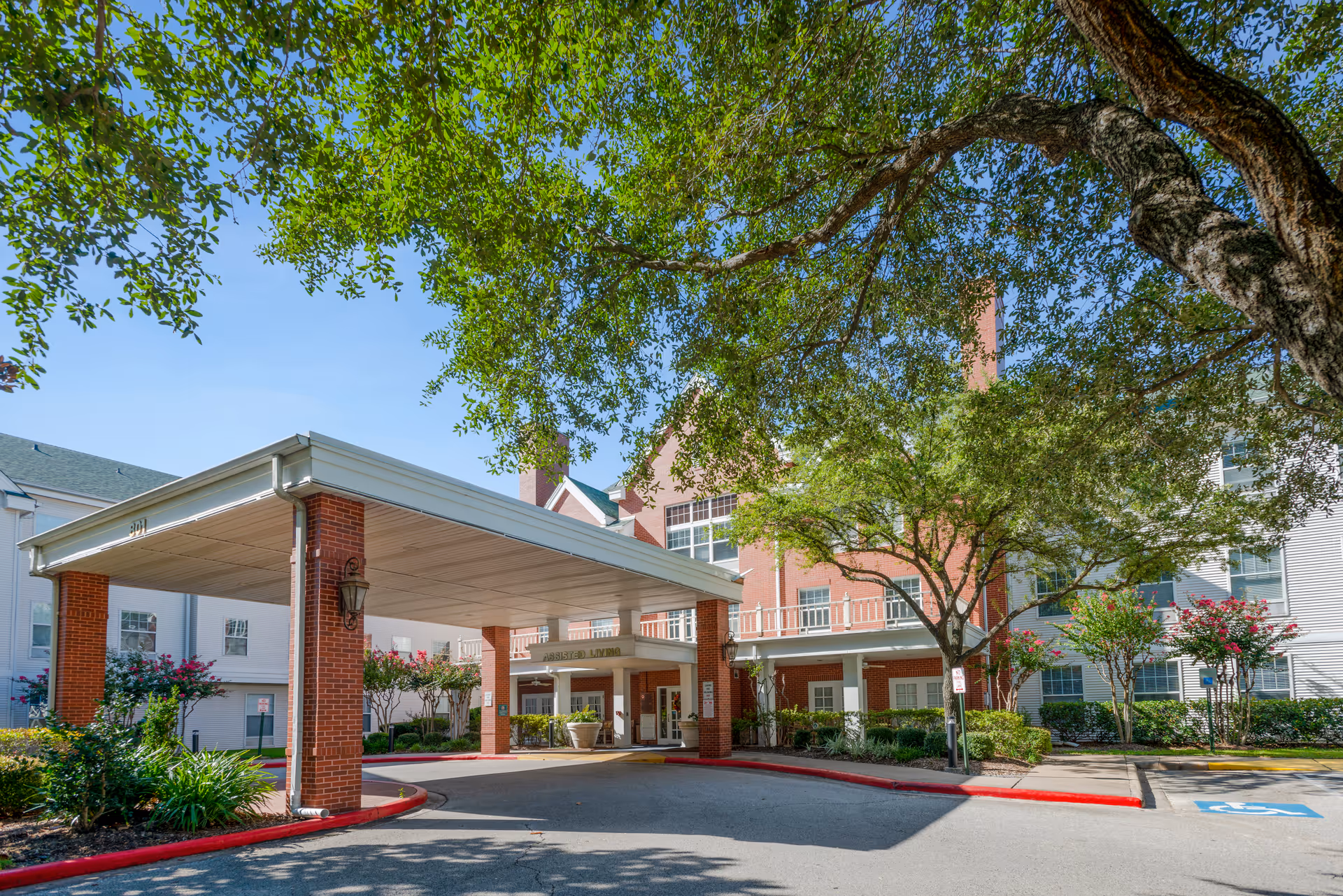 Covered entrance and porte-cochere of a red-brick senior living building with trees and landscaped grounds.