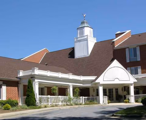 Brick senior living facility with a white entrance porch and cupola against a blue sky.