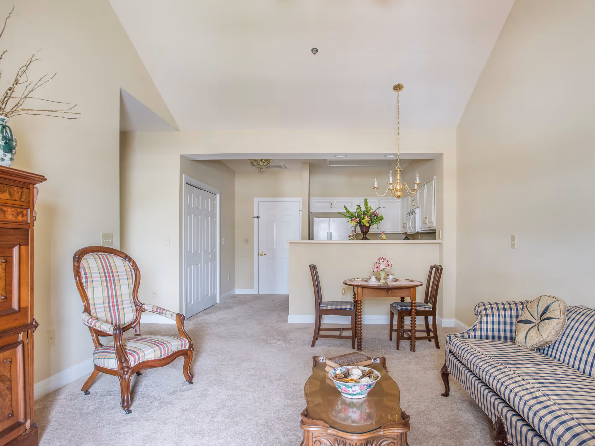 A bright living room and dining area with upholstered chairs, a small round dining table, coffee table, and a kitchen pass-through.