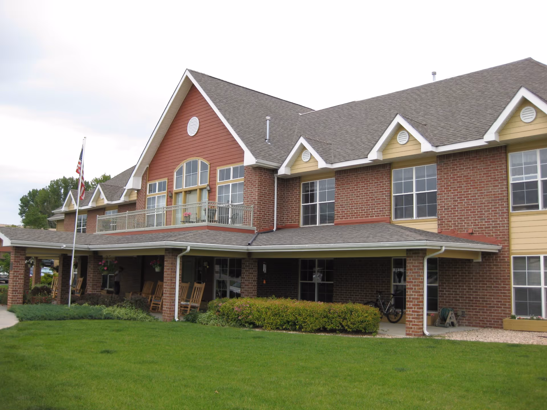 Front exterior of a two-story brick assisted living building with a covered porch, balcony, and lawn.