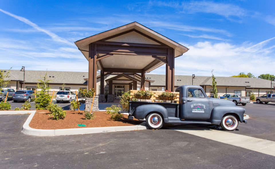 Covered entrance of a memory care community with a vintage pickup truck carrying plants parked in front.