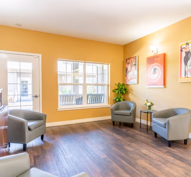 Bright common sitting area with several armchairs, a window, wall art and a small side table.