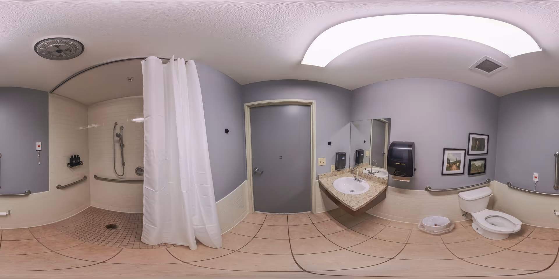 Accessible restroom with a roll-in shower and curtain, wall-mounted sink and mirror, toilet with grab bars and tiled floor.