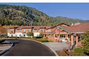 Curved driveway leading to the entrance of a red-roofed senior living building with an American flag and forested hills behind it.