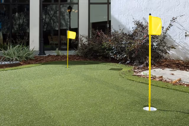 Outdoor putting green with two yellow flags near a building and windows.