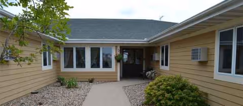 Exterior entrance of The Beacon at Lake Crystal, a single-story beige senior facility with a walkway.