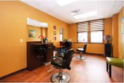 Small salon room with two styling chairs, mirrors, a window with blinds, and warm orange walls.