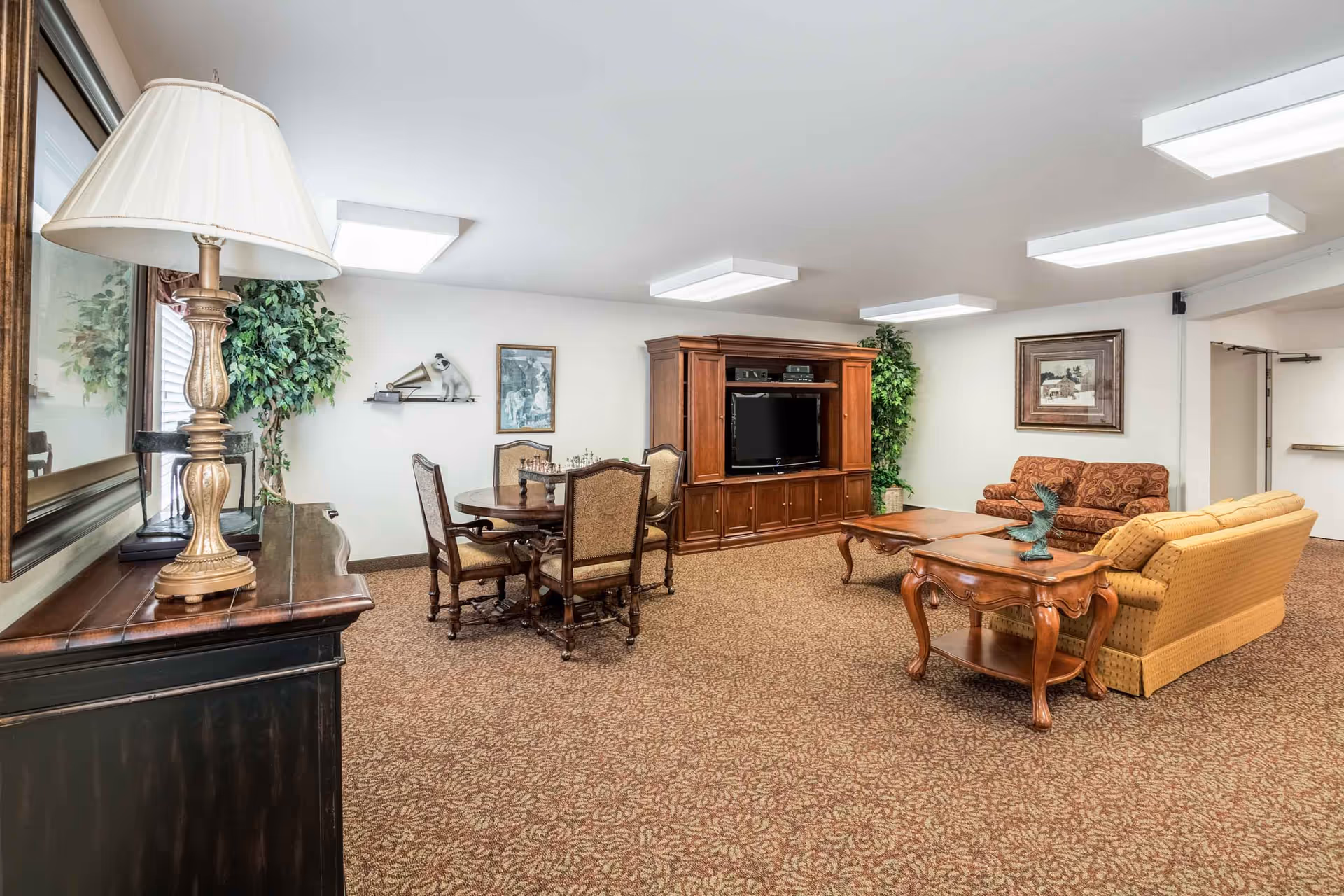 Well-lit common living room with sofas, a coffee table, a TV entertainment center, and a dining table with chairs.