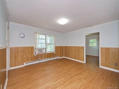 Empty living room with wood paneling, light blue walls, window air conditioner, and doorway.