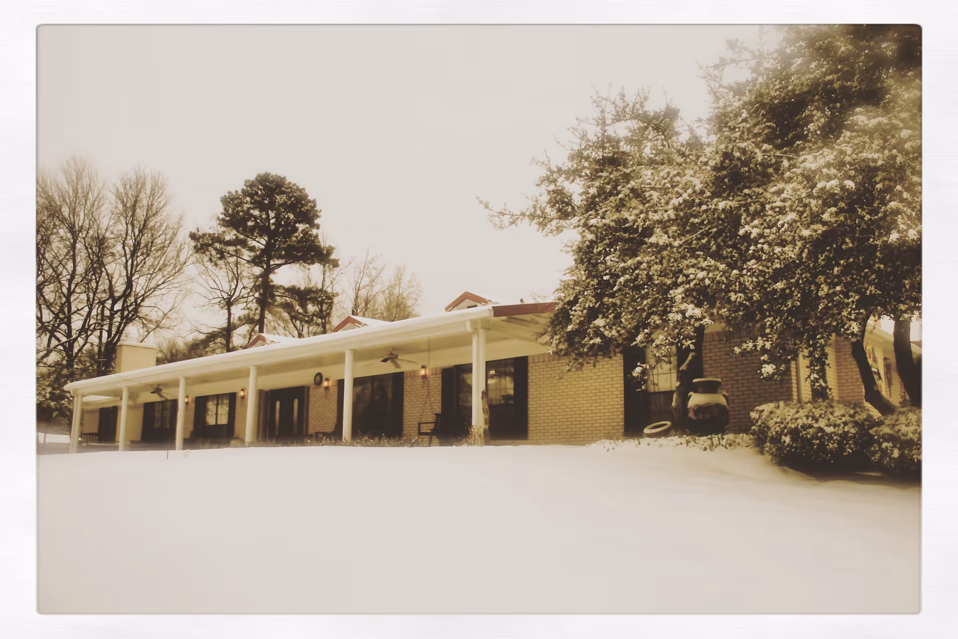 Snow-covered front of a single-story brick building with a covered porch and surrounding trees.