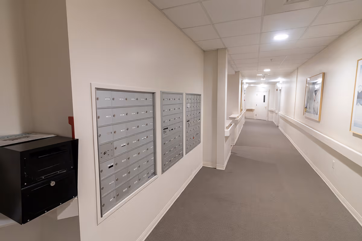 Well-lit interior hallway with wall-mounted mailboxes, handrails, and framed artwork.