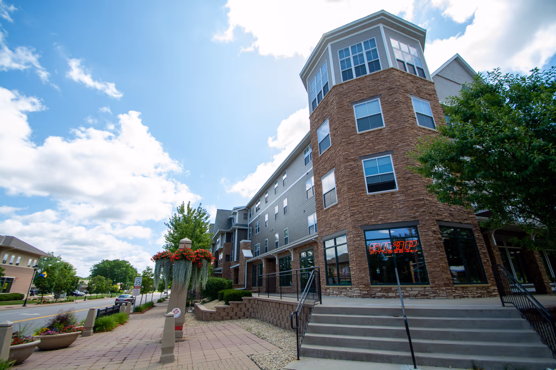 Front exterior of a multi-story stone-and-siding building with steps, planters, and a blue sky.