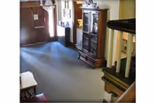 Carpeted entrance lobby with double front doors, a wooden display cabinet, staircase railing and seating.
