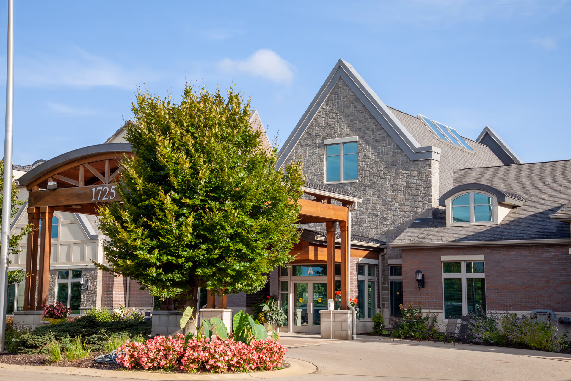Front entrance of a brick and stone senior living building with a covered porte-cochere, landscaping, and the number 1725 on the arch.