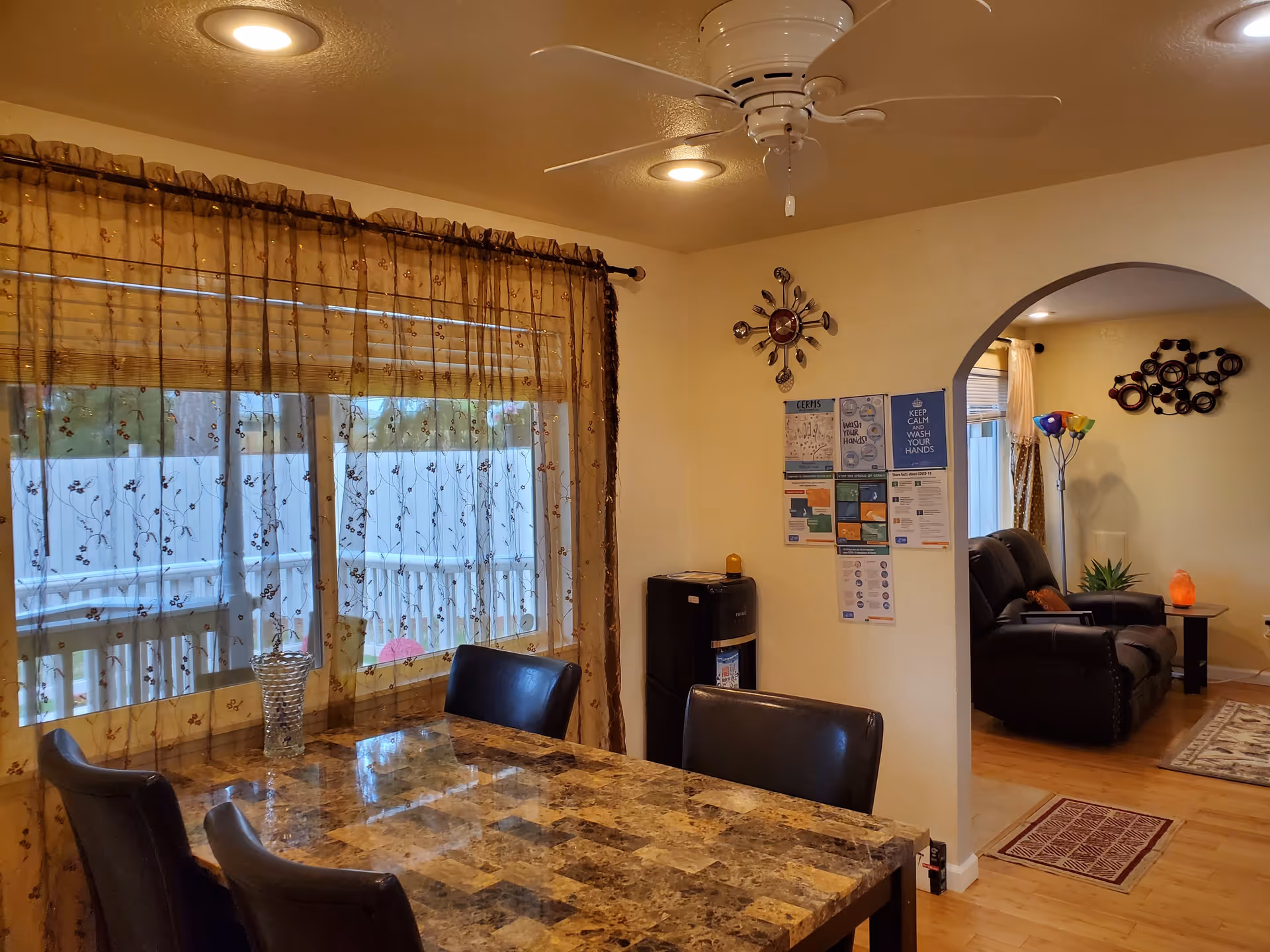 Dining area with a marble-patterned table and chairs by a curtained window, an archway opening to a living room with recliners.