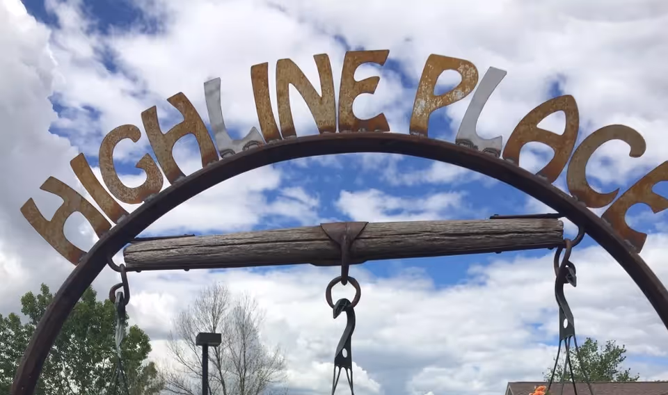 A rustic metal arch sign that reads 'HIGHLINE PLACE' against a cloudy blue sky.