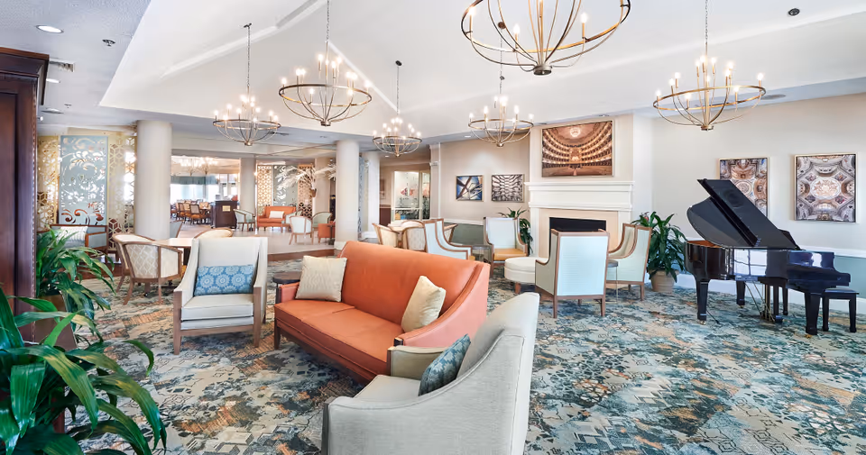 Bright communal lounge with sofas and armchairs, chandeliers, a fireplace and a grand piano.