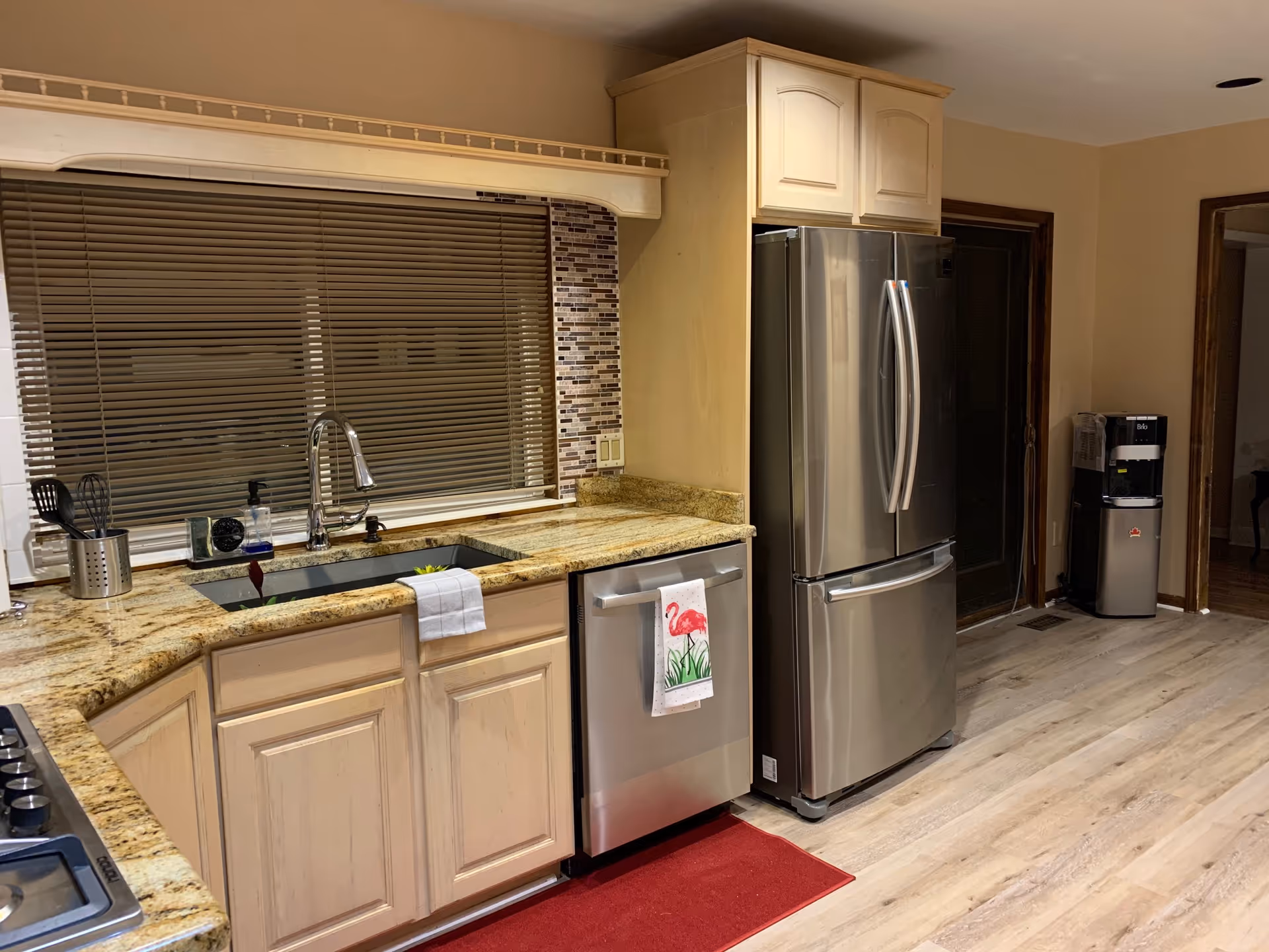 Spacious kitchen with granite countertops, sink under a window with blinds, and stainless steel refrigerator and dishwasher.
