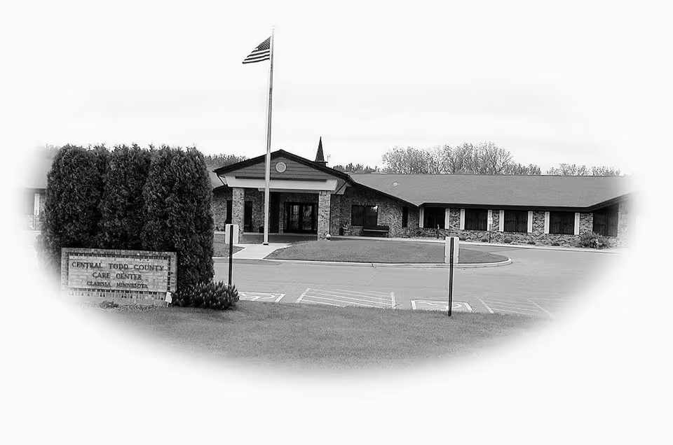 Front exterior of Central Todd County Care Center with a flagpole, circular driveway, and a sign in the foreground.