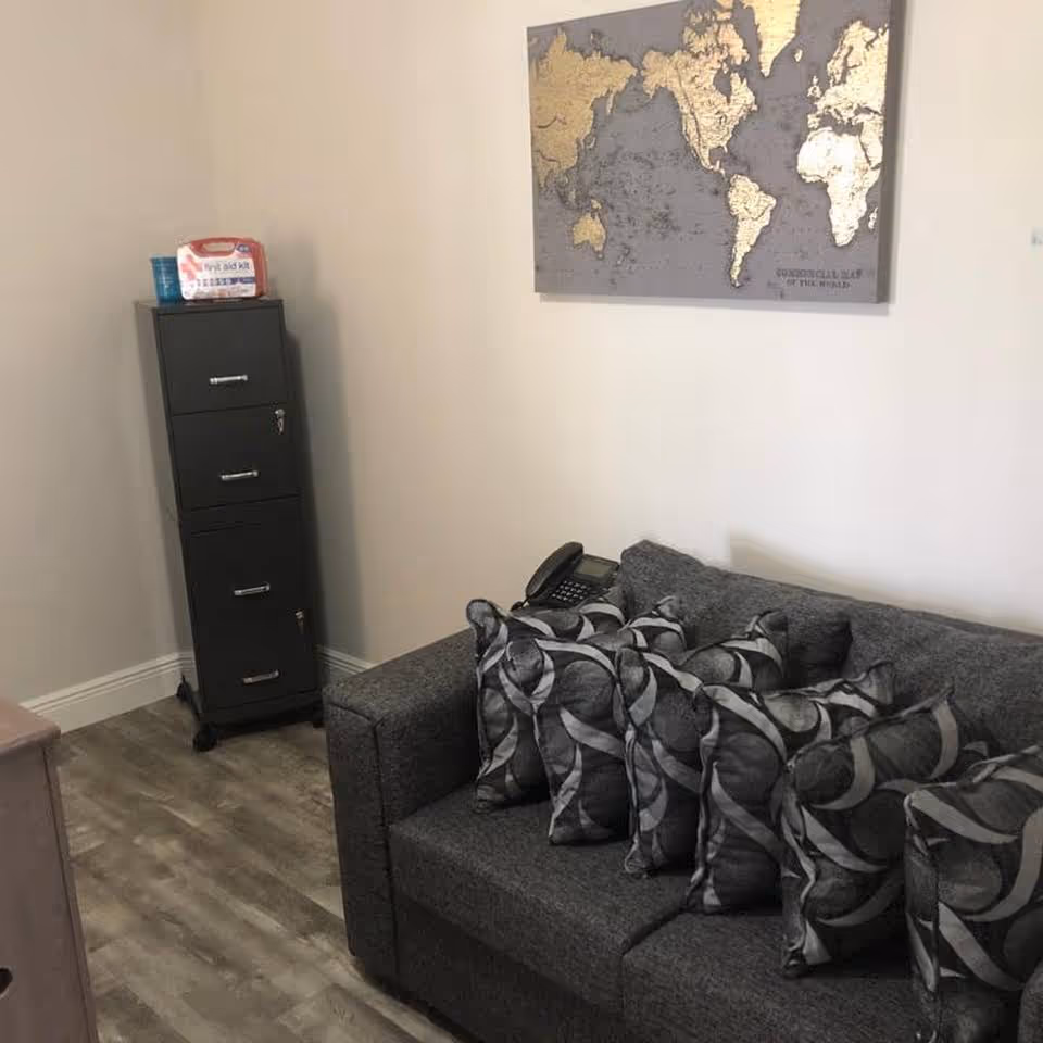 A small sitting area with a gray sofa covered in patterned pillows, a phone on the arm, a tall black filing cabinet in the corner, and a world map on the wall.