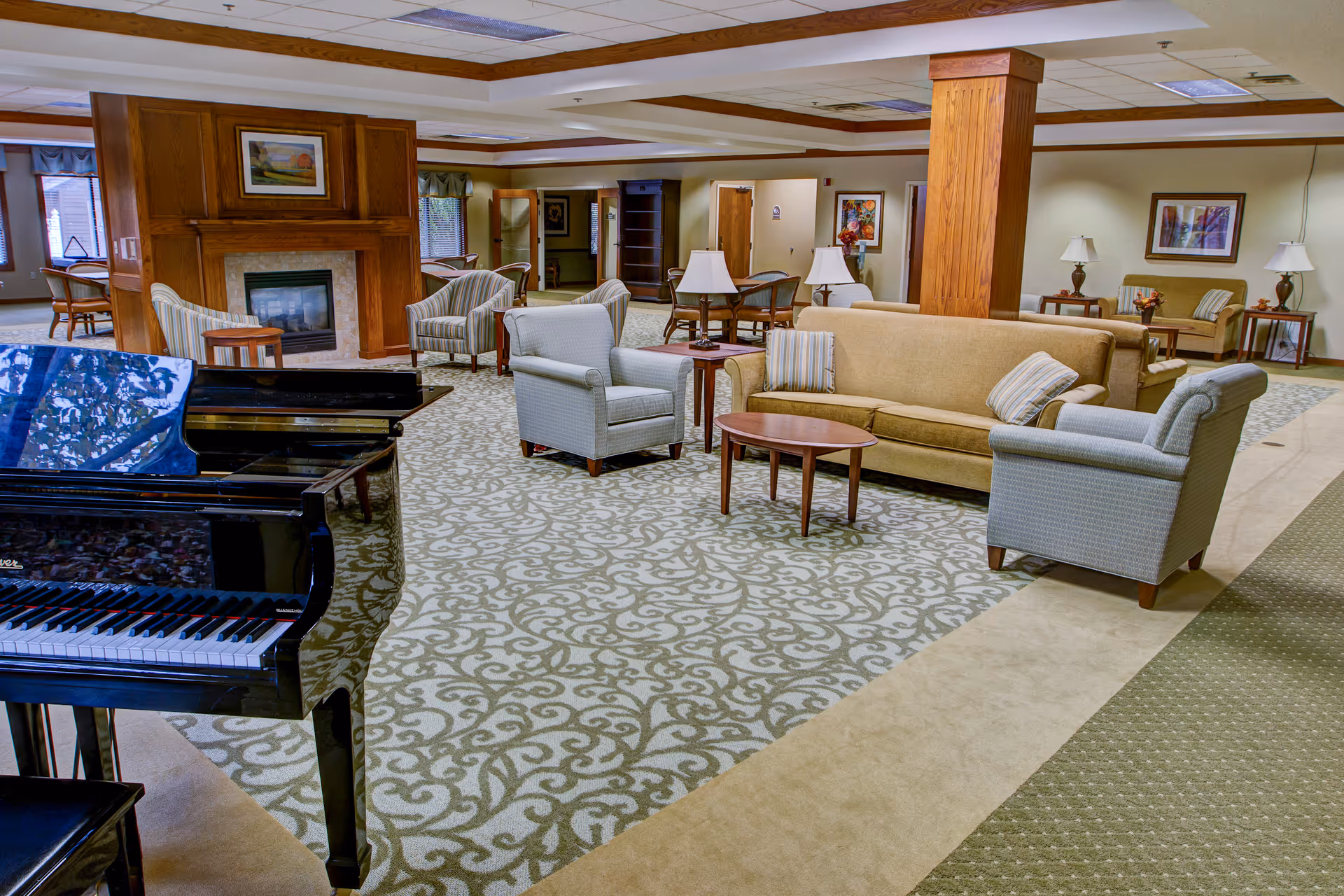 Spacious senior living common lounge with a grand piano, sofas and armchairs arranged around tables and a fireplace.