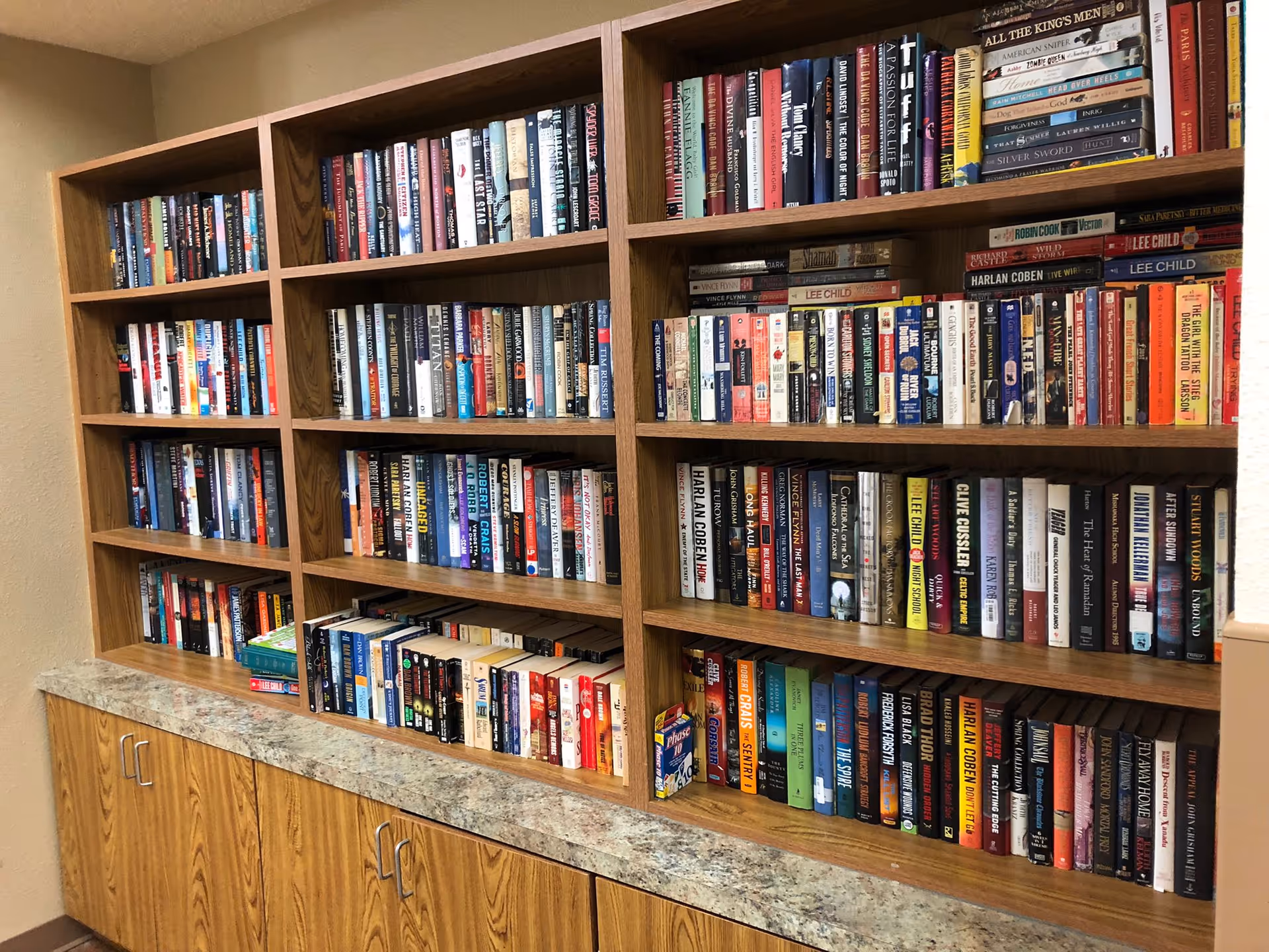 Wooden built-in bookshelves filled with rows of books above a laminate countertop and cabinets.