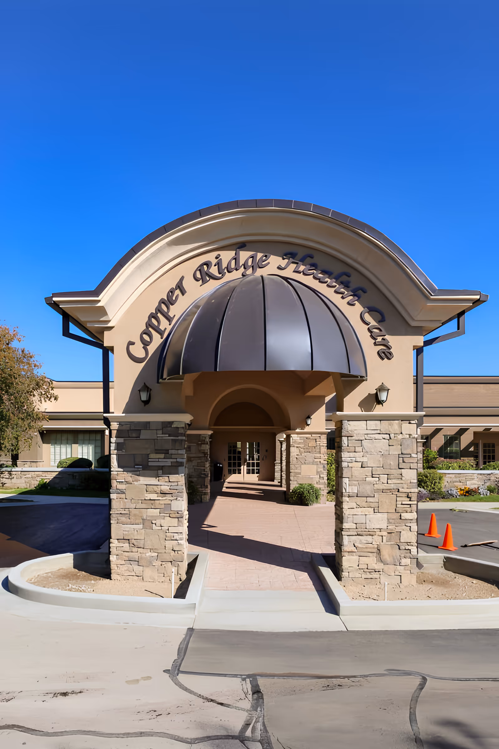 Entrance of Copper Ridge Health Care showing a stone-columned archway with a metal canopy under a clear blue sky.