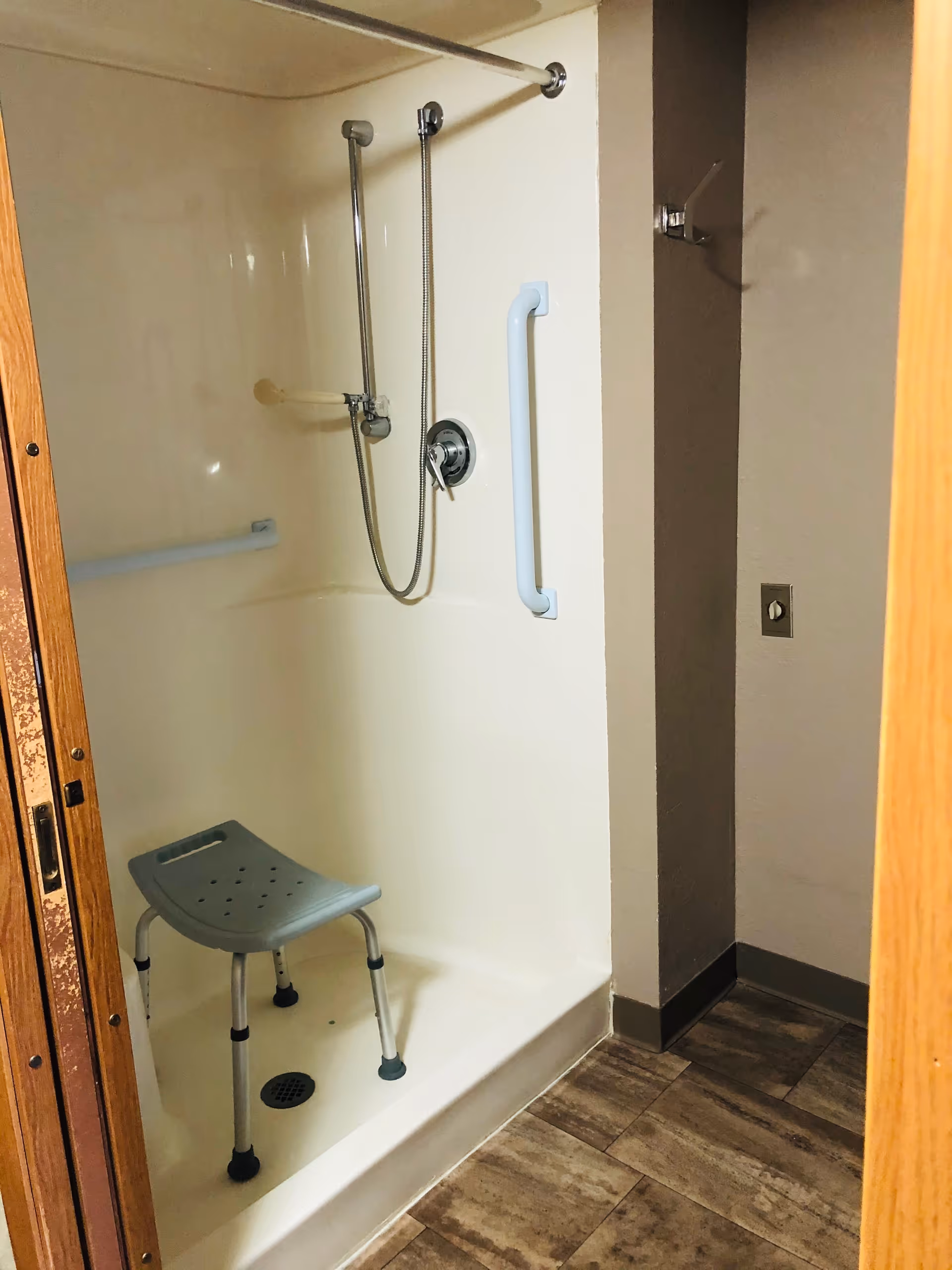 Accessible shower stall with grab bars, a handheld showerhead, and a gray shower chair.