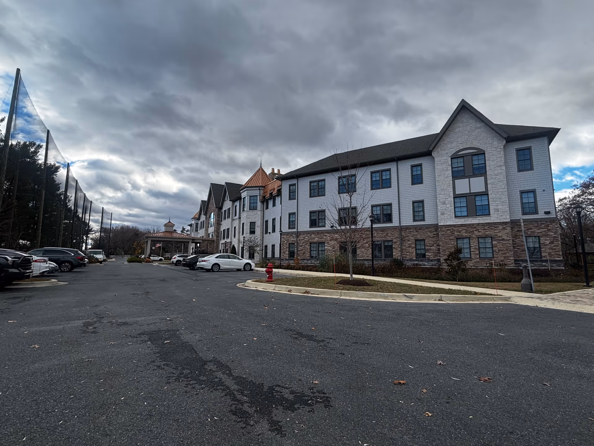 Front exterior of a multi-story senior living building with parked cars in the driveway under a cloudy sky.