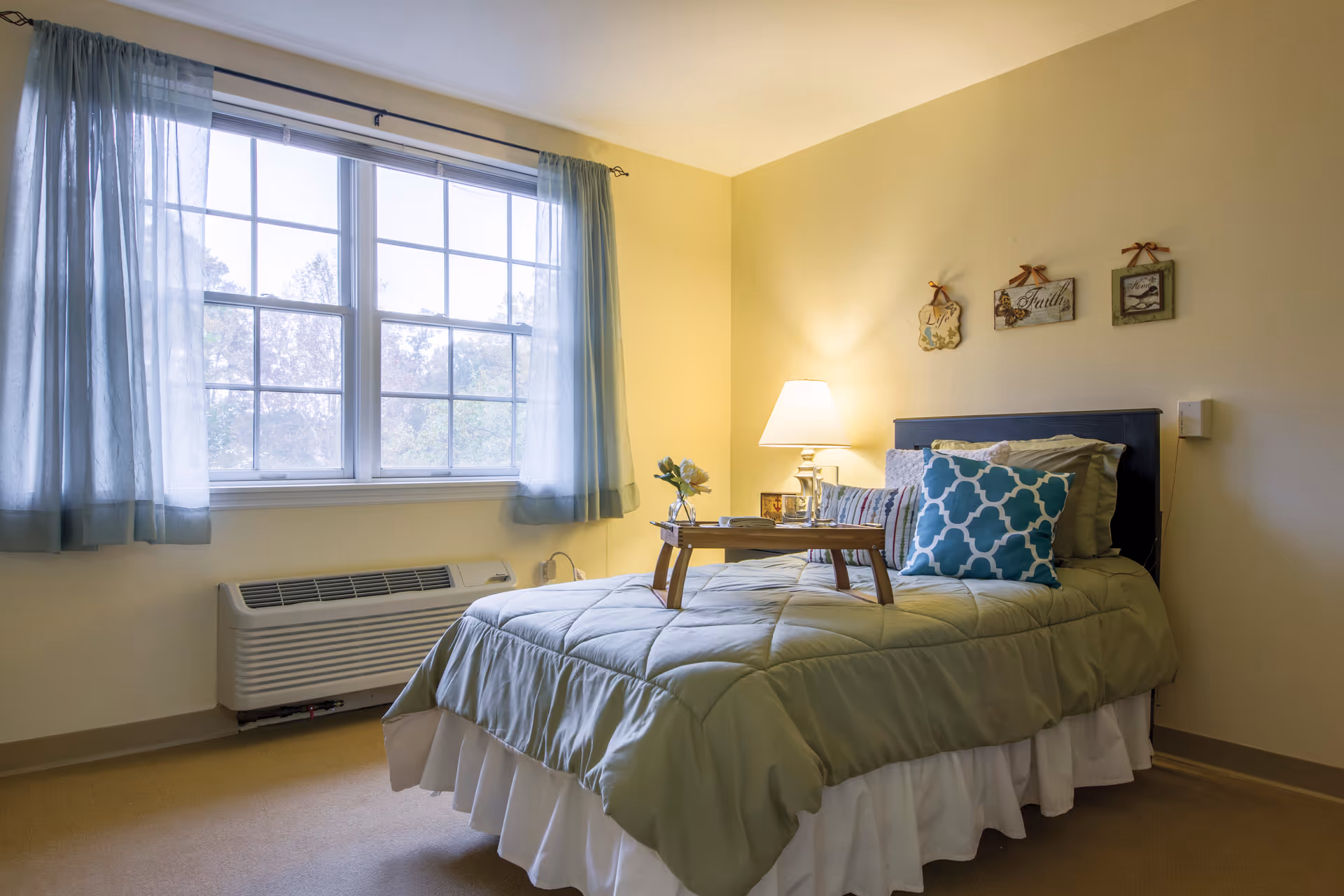 Bright bedroom in Brookdale Durham senior living facility with bed, tray, and window.