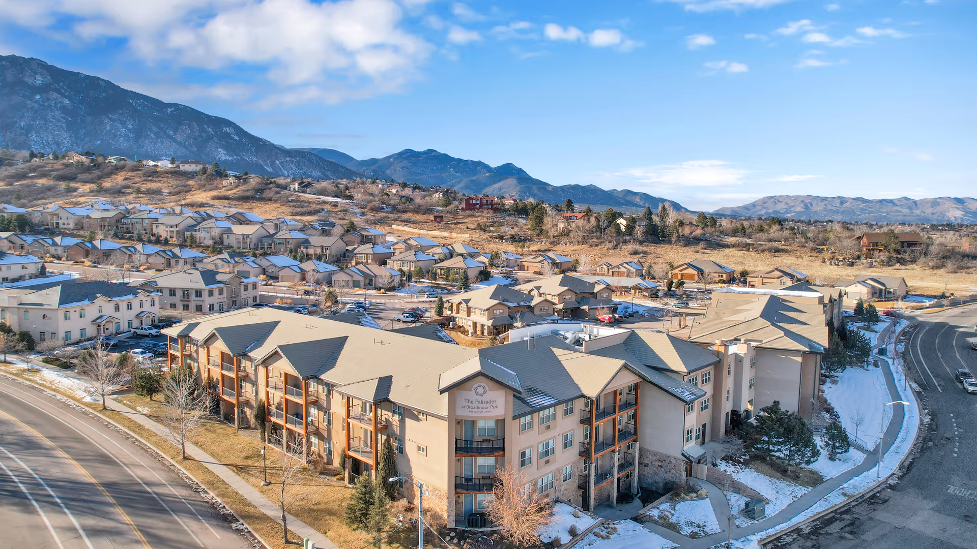 Aerial view of a multi-story senior living building and adjacent neighborhood with mountains in the background.