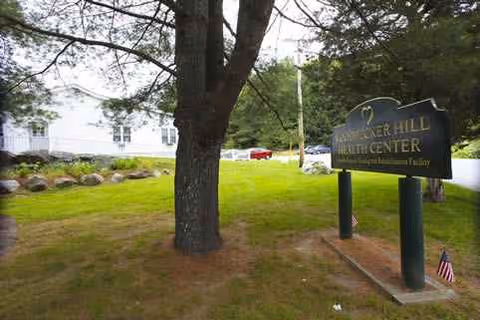 Woodpecker Hill Health Center sign on a grassy lawn with trees and a building behind
