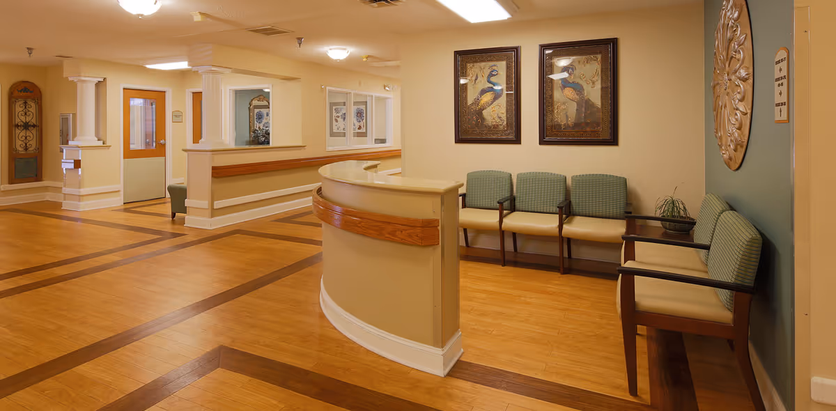 Reception/waiting area with a curved front desk, rows of chairs, framed artwork, and wood flooring.