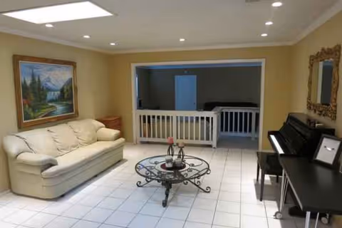 Bright living room with cream sofa, glass coffee table, piano, and wall art.