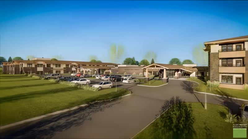 Exterior view of a senior living facility with a curved driveway, parking lot, and low-rise buildings under a clear blue sky.