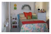 Small bedroom with a colorful bed, multiple pillows, a white dresser, and wall decorations.