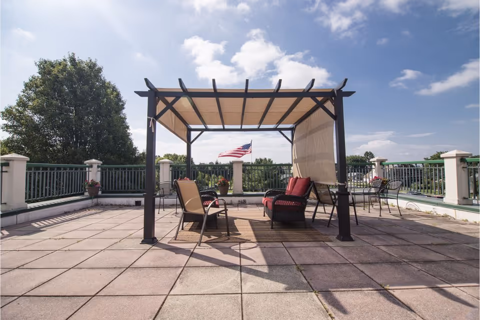 Rooftop terrace with a pergola-covered seating area, chairs and tables, and an American flag in the background.