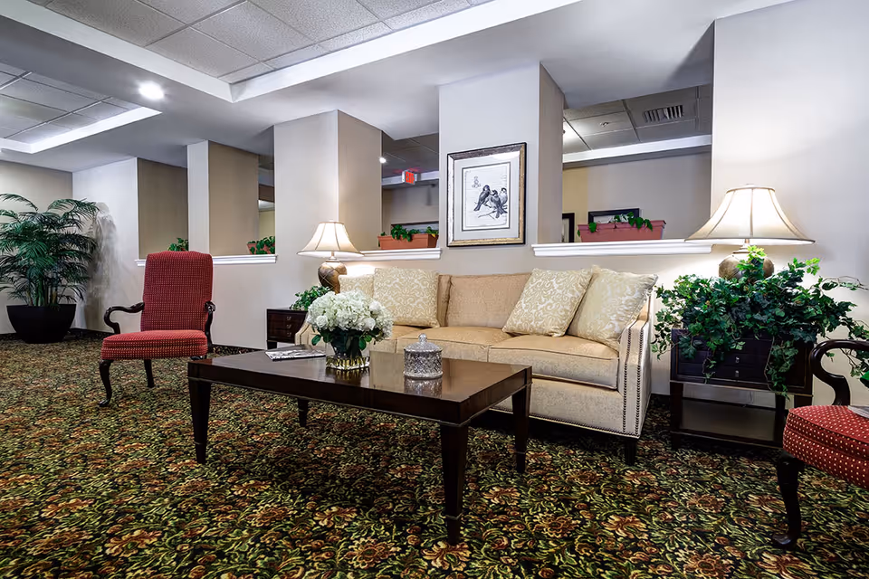A cozy lounge area featuring a sofa, decorative chairs, and plants in a senior living facility.