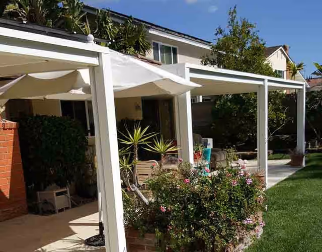 Exterior view of a senior living facility with white pergola-covered patios, greenery, and lawn.