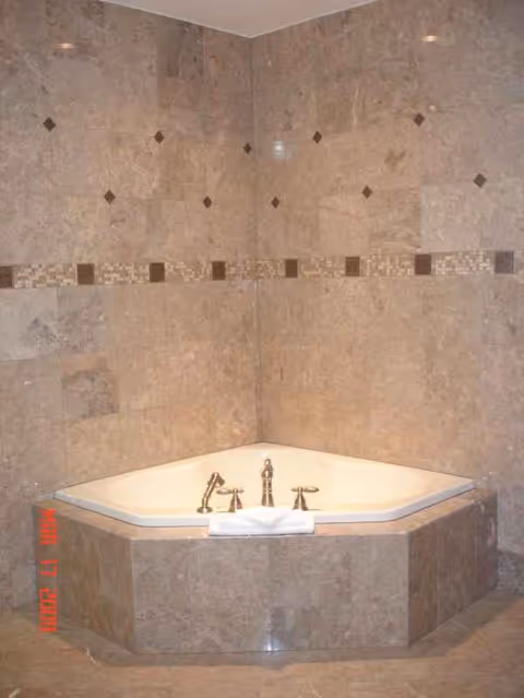 Marble-tiled bathroom featuring a corner built-in bathtub with brass fixtures.