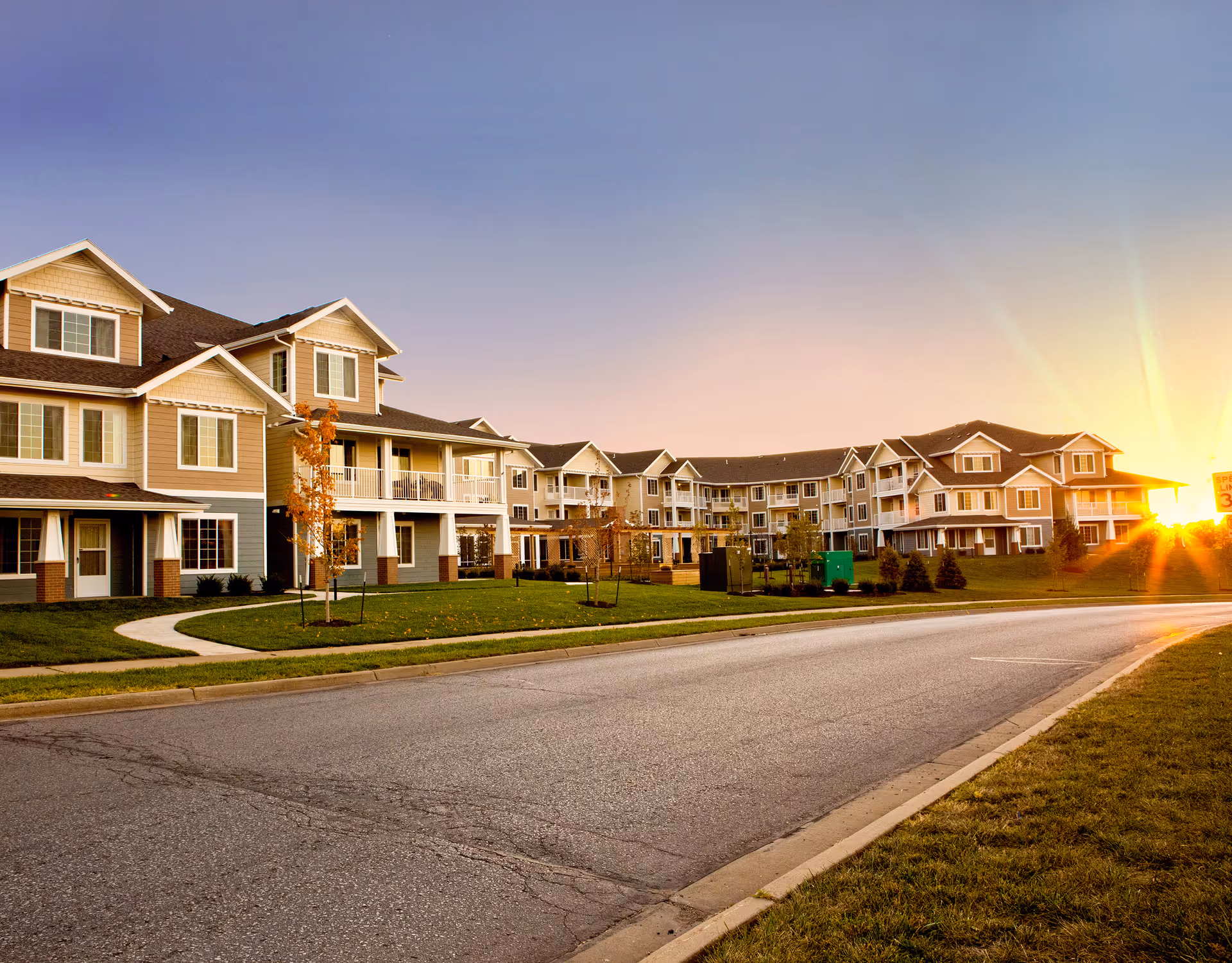 Row of beige senior living buildings along a curved street at sunset.